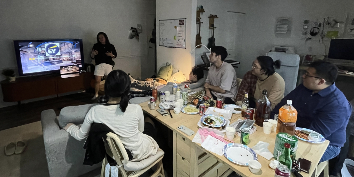 A group of friends sitting on a messy table full of snacks watching a life update presentation.